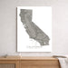 A vertical wall art print showing a grayscale topographic map of California with the word CALIFORNIA at the bottom, displayed above a wooden console table against a light textured wall.