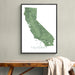 A framed vertical map print of California in green tones with the word CALIFORNIA at the bottom, hanging on a light gray wall above a wooden bench with a draped cream throw.