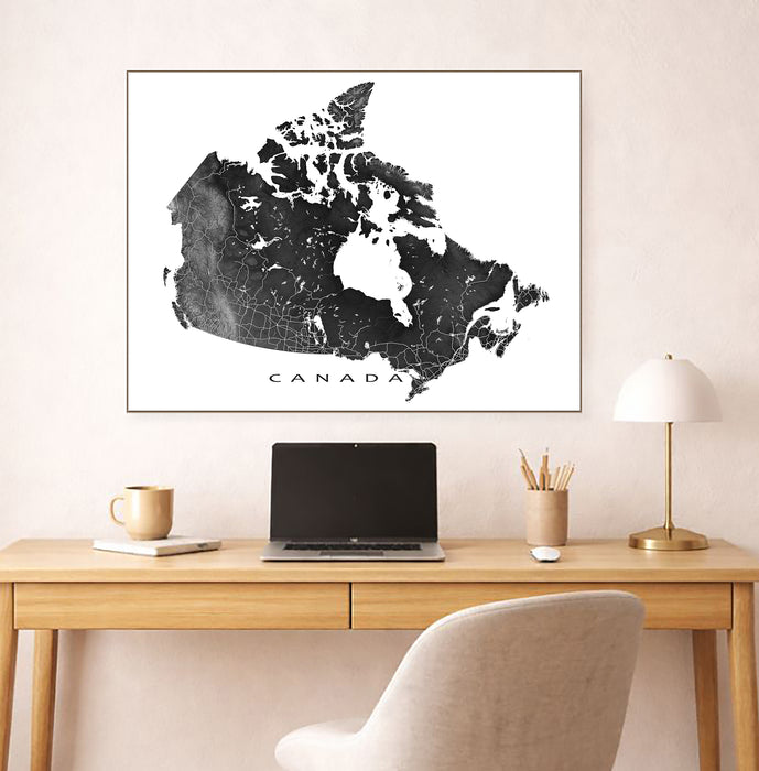 Framed map of Canada on a wall above a desk with a laptop and lamp.