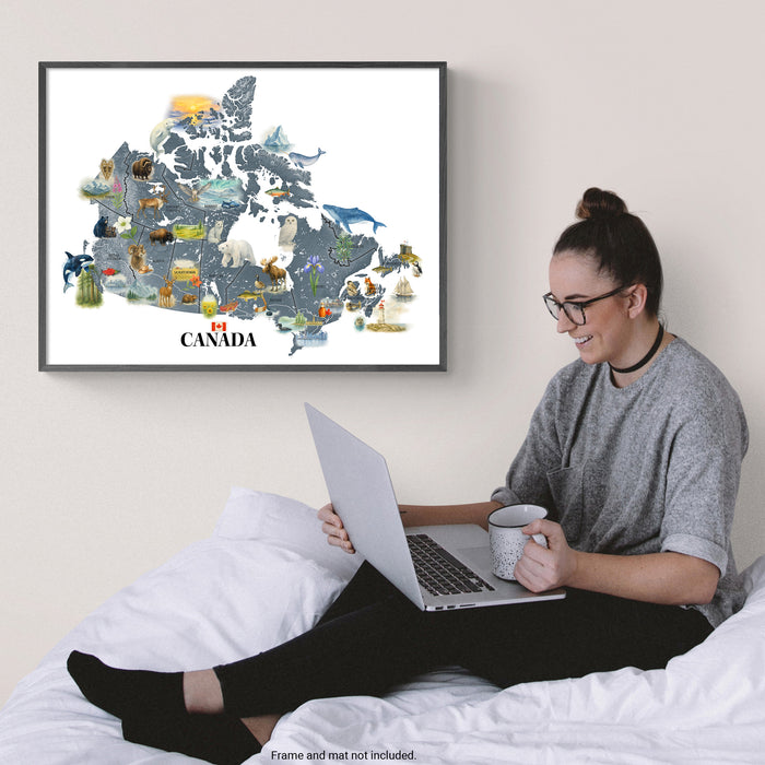 Woman sitting on a bed using a laptop with a framed map of Canada on the wall.