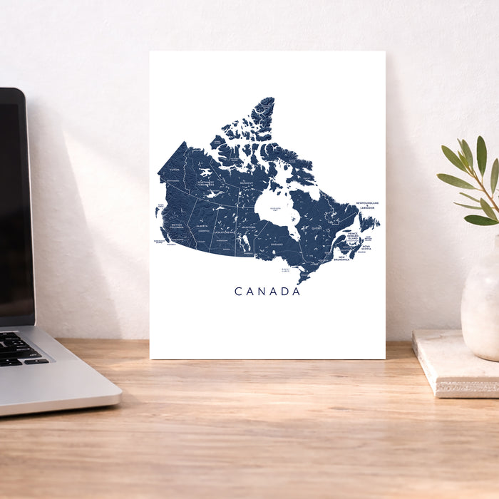 Map of Canada on a white wall next to a laptop on a wooden desk.