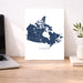 Map of Canada on a white wall next to a laptop on a wooden desk.