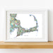 Framed map of Cape Cod on a white wall with a wooden shelf.