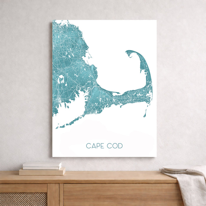 Map of Cape Cod in teal and white on a light gray wall above a wooden shelf.