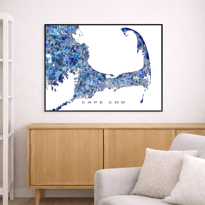 Framed map of Cape Cod with blue abstract design above a wooden cabinet and white sofa.