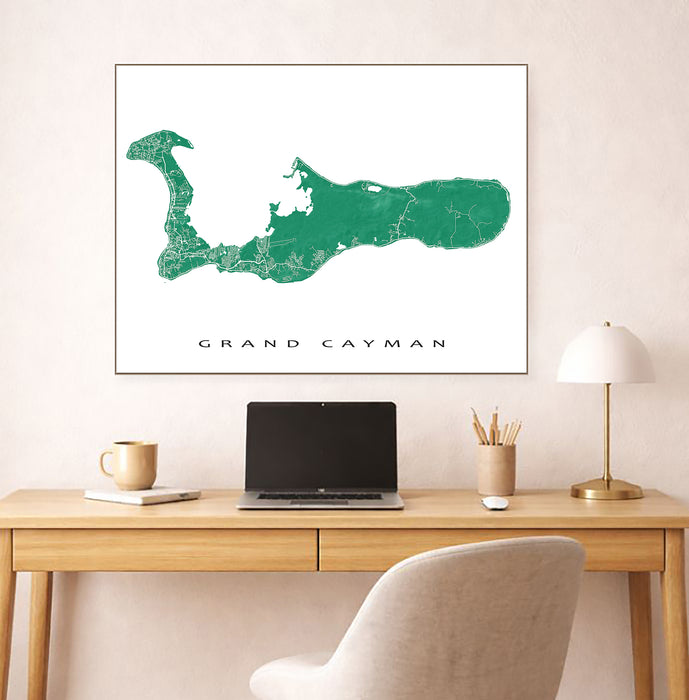 Framed map of Grand Cayman on a wall above a desk with a laptop and lamp.