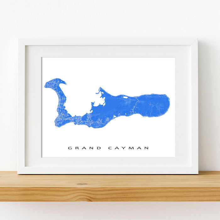 Framed map of Grand Cayman on a white wall with a wooden shelf.