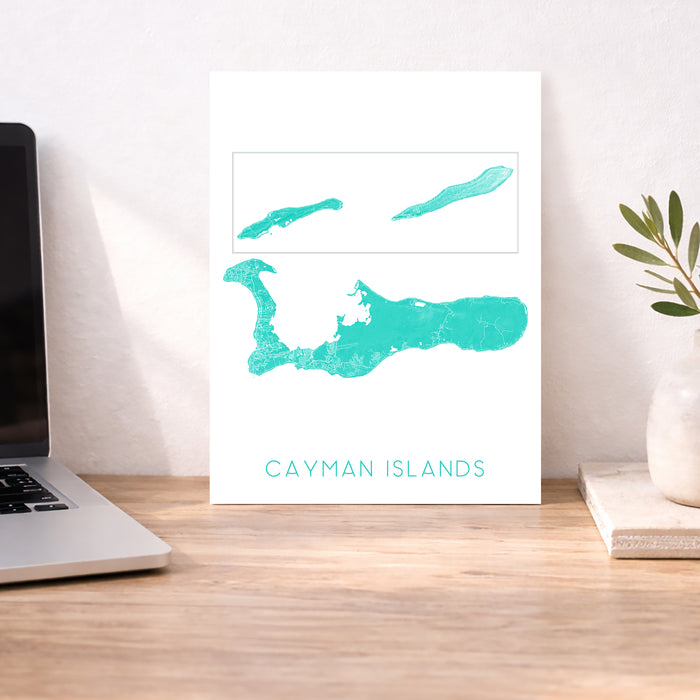Map of Cayman Islands on a white background next to a laptop on a wooden desk.