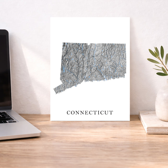 Map of Connecticut on a white background with a laptop and plant in the background.