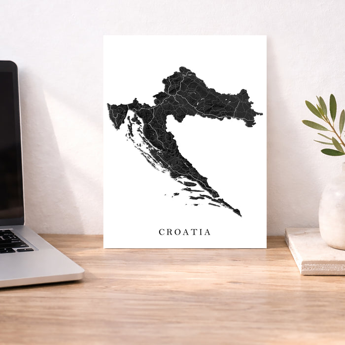 Map of Croatia on a white background next to a laptop on a wooden desk.
