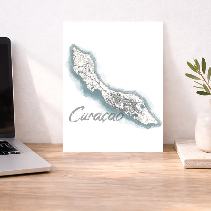 Map of Curacao on a desk with a laptop and plant.
