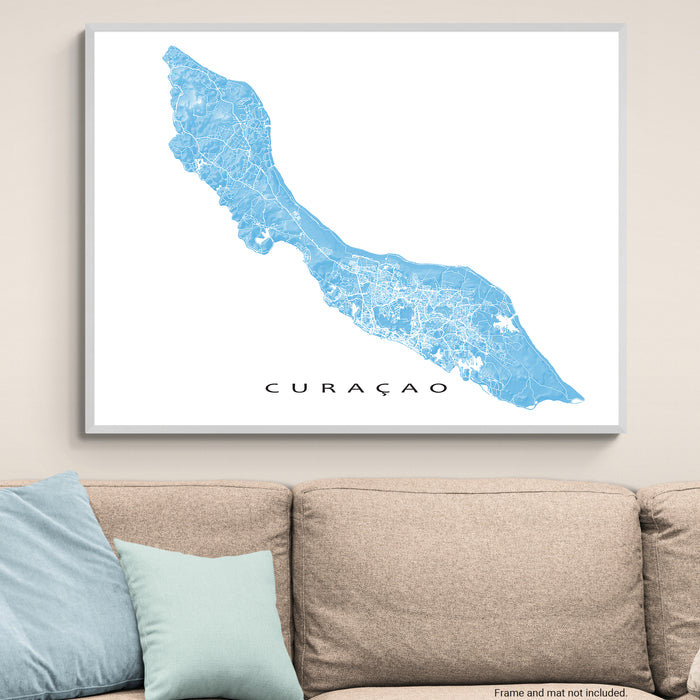 Framed map of Curaçao on a wall above a beige sofa with light blue pillows.