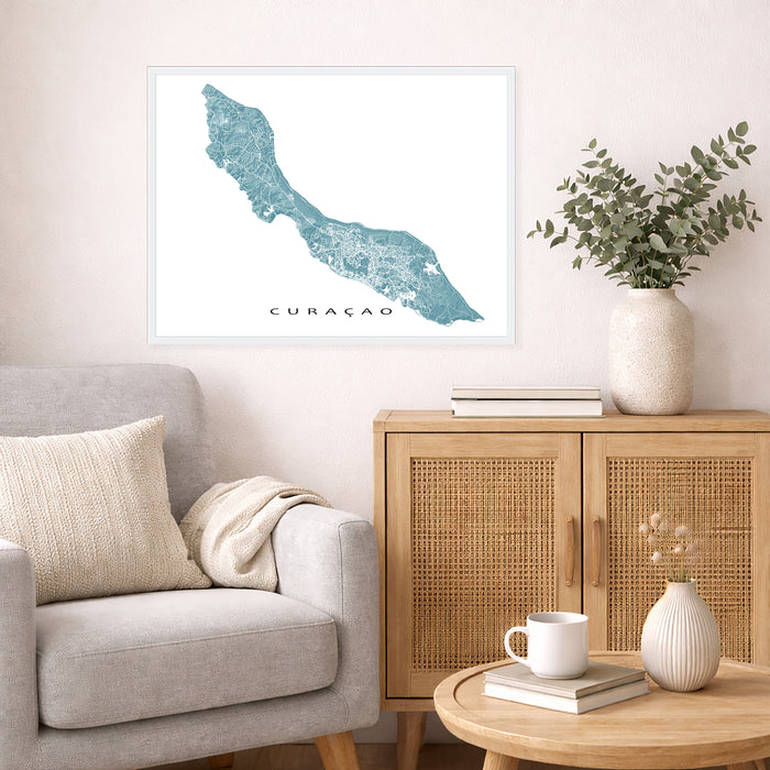 Living room with a map of Curaçao on the wall, a vase with plants, and a coffee table with books and a mug.
