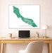 Framed map of Curacao on a wall above a desk with a laptop and lamp.