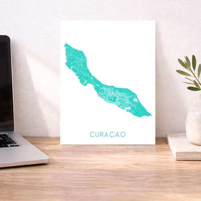 Map of Curacao on a white background next to a laptop on a wooden desk.