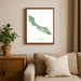 Framed map of Curacao on a wall above a sofa with a plant beside it.