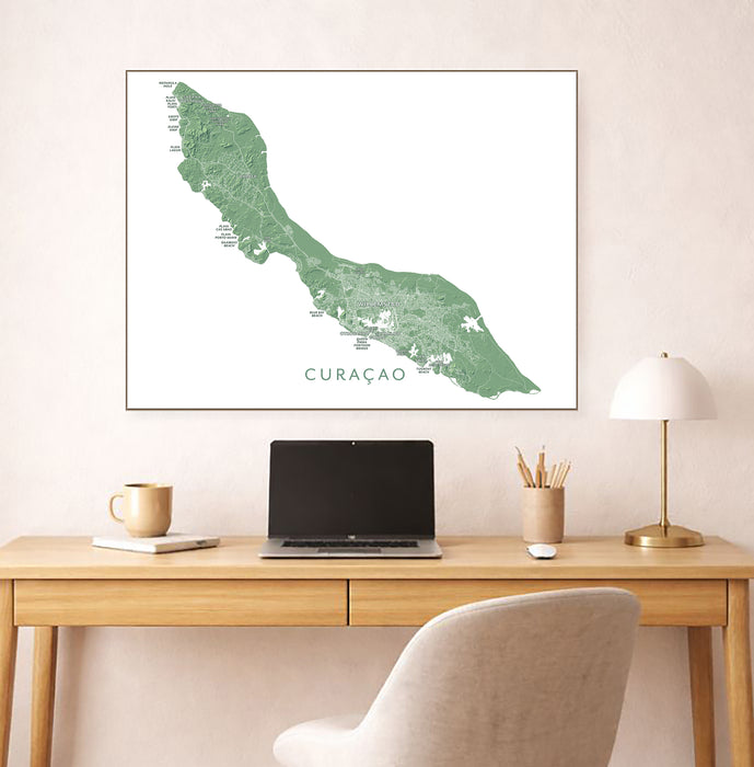 Framed map of Curacao on a wall above a desk with a laptop and lamp.