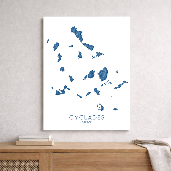 Map of Cyclades Islands, Greece on a white background, displayed on a wall above a wooden shelf.