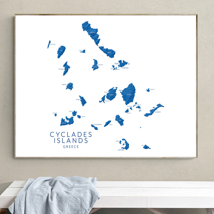 Framed map of Cyclades Islands, Greece on a wall above a white bench.