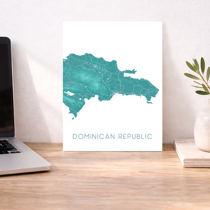 Map of the Dominican Republic on a white background next to a laptop on a wooden desk.