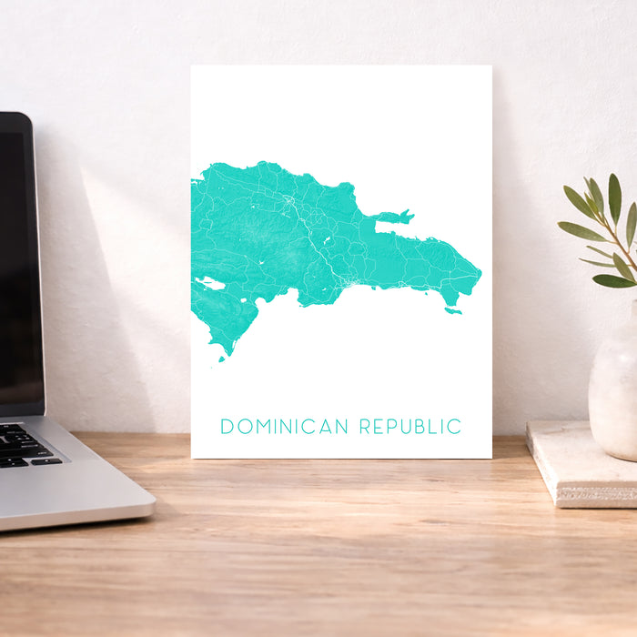 Map of the Dominican Republic on a white background, displayed on a wooden desk with a laptop and plant.