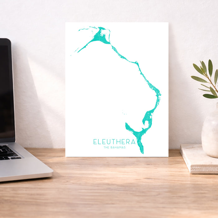 Teal map of Eleuthera, The Bahamas on a white background, displayed on a wooden desk.