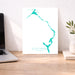 Teal map of Eleuthera, The Bahamas on a white background, displayed on a wooden desk.
