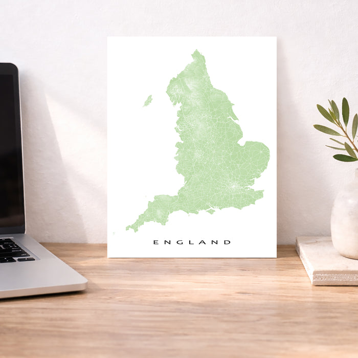Map of England on a white background next to a laptop on a wooden desk.