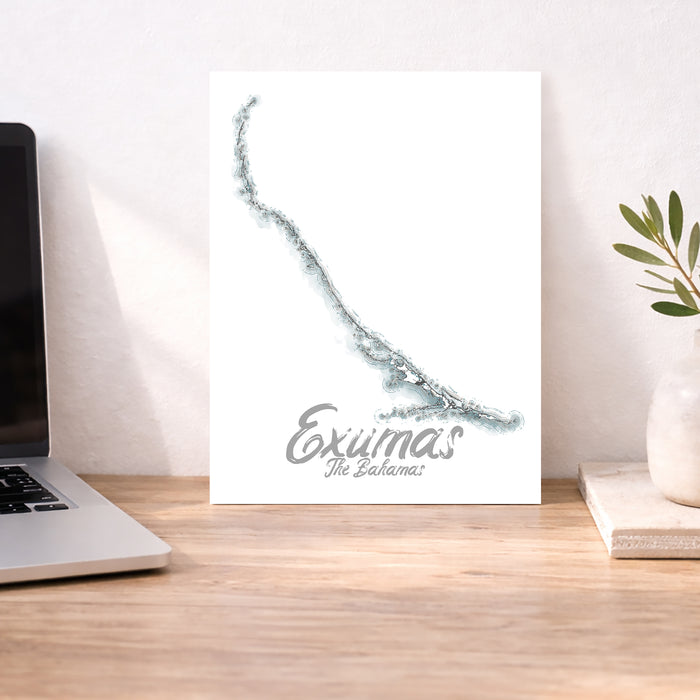 Desk with a laptop, plant, and map of Exuma, The Bahamas on a white wall.