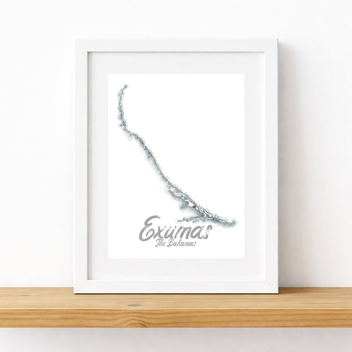 Framed map of Exumas on a white wall with a wooden shelf below.