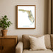 Framed map of Florida on a wall above a beige sofa with a plant beside it.