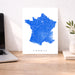 Map of France on a white background next to a laptop on a wooden desk.