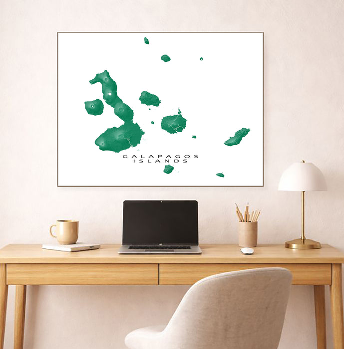 Framed map of Galapagos Islands on a wall above a desk with a laptop and lamp.
