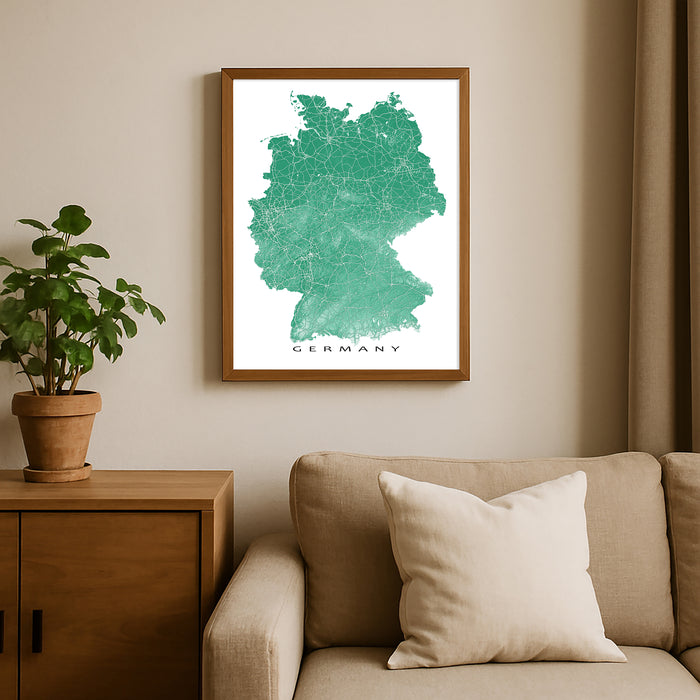 Framed map of Germany on a wall above a beige sofa with a plant beside it.