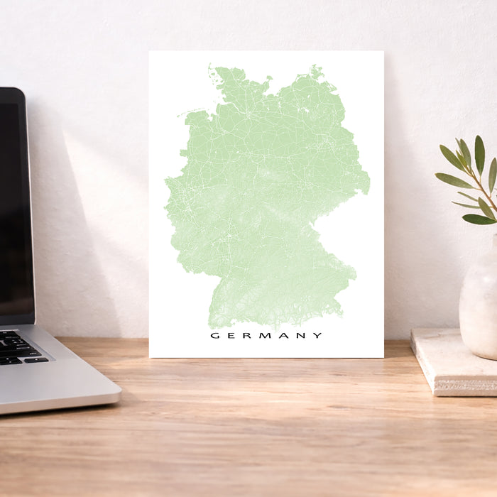 Map of Germany on a white background next to a laptop on a wooden desk.
