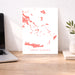 Map of Greek Islands on a white background displayed on a wooden desk with a laptop and plant.