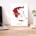 Map of Greece on a white background next to a laptop on a wooden desk.