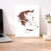 Map of Greece on a white background next to a laptop on a wooden desk.