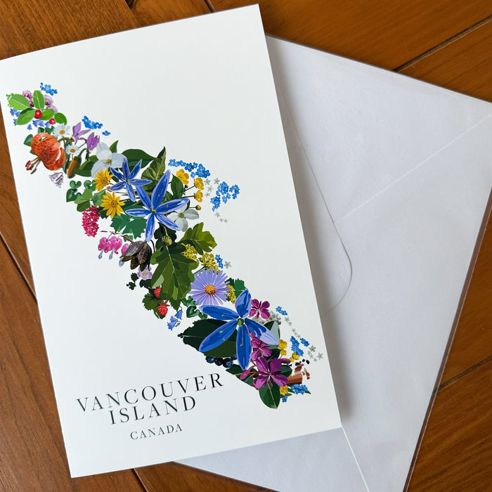 A white Vancouver Island card featuring a colorful floral map design and the text 'VANCOUVER ISLAND CANADA,' placed on a wooden surface with a white envelope behind it.