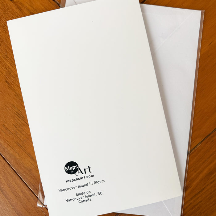 A white back side of a greeting card with the Maps As Art logo printed at the bottom, placed on top of a white envelope on a wooden surface.