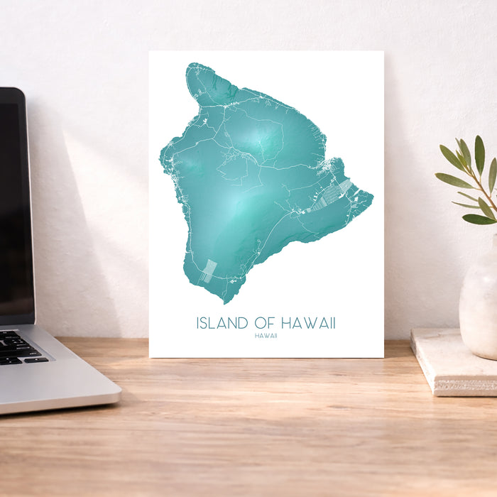 Map of the Island of Hawaii on a white background next to a laptop on a wooden desk.