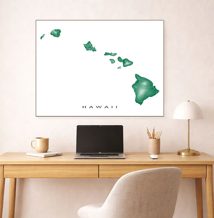 Framed map of Hawaii on a wall above a desk with a laptop and lamp.