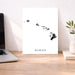 Poster with 'HAWAII' text on a desk next to a laptop and plant