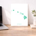 Desk with a laptop, a print of Hawaii's map, and a plant.
