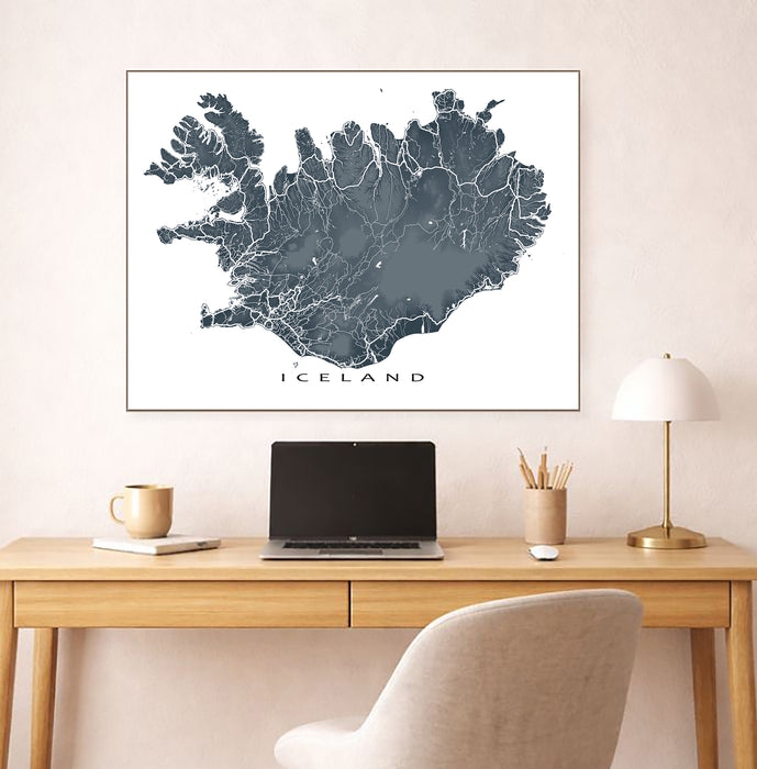Framed map of Iceland on a wall above a desk with a laptop and lamp.