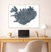 Framed map of Iceland on a wall above a desk with a laptop and lamp.