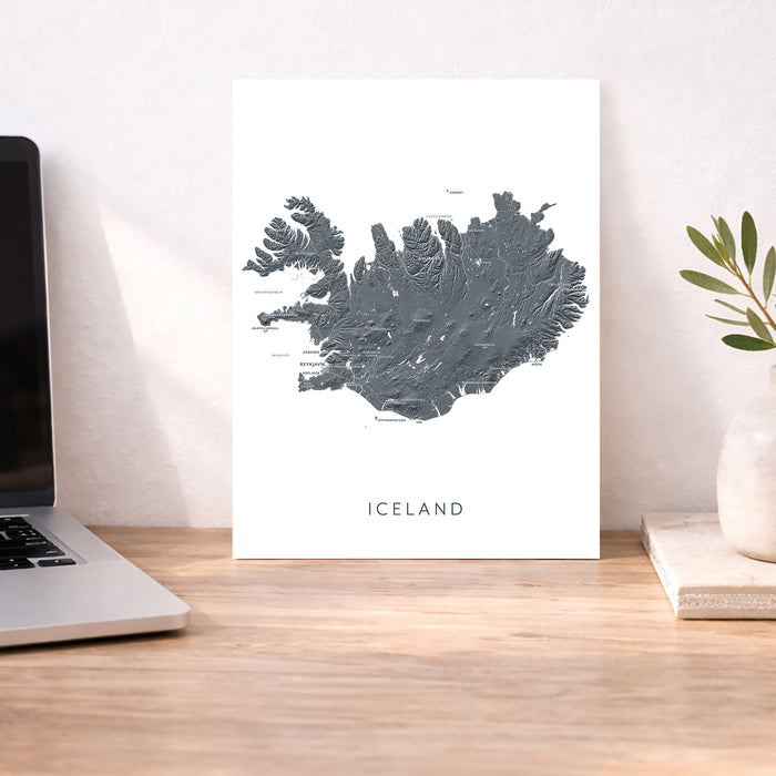 Map of Iceland on a white background next to a laptop on a wooden desk.