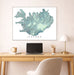 Framed map of Iceland on a wall above a desk with a laptop and lamp.
