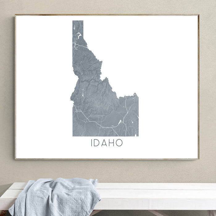 Framed map of Idaho on a wall above a white bench with a gray blanket.