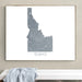 Framed map of Idaho on a wall above a white bench with a gray blanket.